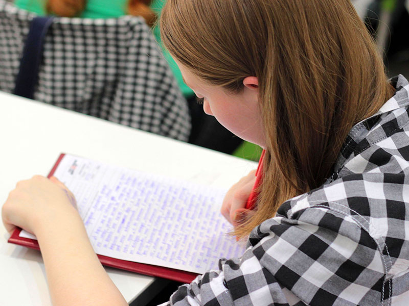 Girl with a plaid shirt writing on paper with a red pen with a Christian Scholarships