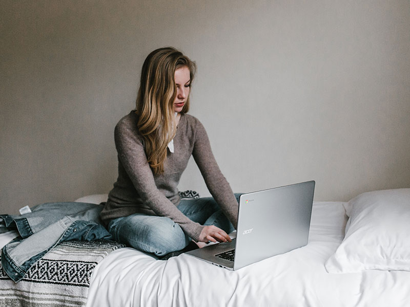 Girl sitting on bed with laptop paying for college
