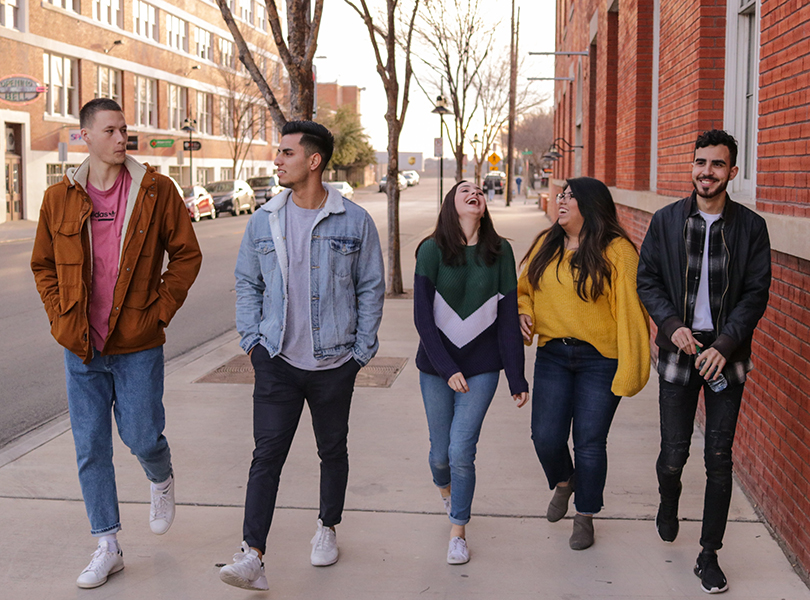 5 college students walking and talking together on a city street