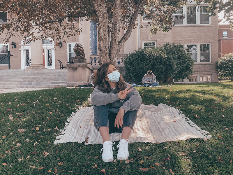 Student sitting with mask on the grass in front of TJ Jones Library