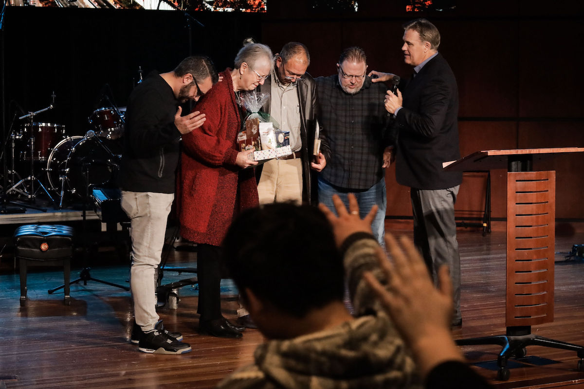 President Scott Hagan prays over retirees Rebecca Norberg and Bob Brenneman