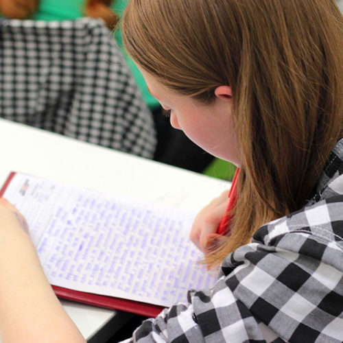 Girl with a plaid shirt writing on paper with a red pen with a Christian Scholarships