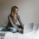 Girl sitting on bed with laptop paying for college
