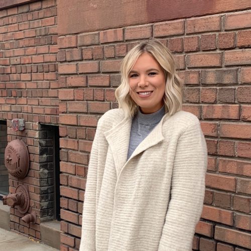 girl in beige sweater in front of brick wall