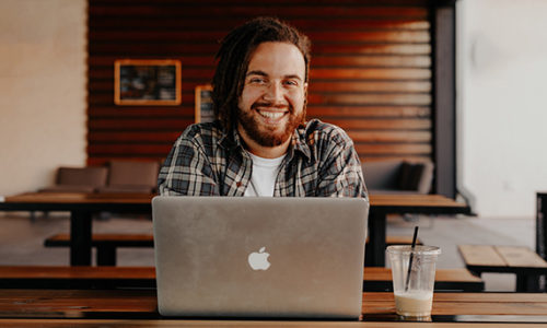 Student smiling at while using laptop in coffee shop