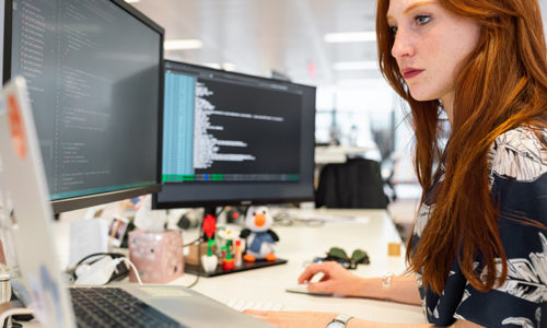 Woman working in front of three computers and writing code.