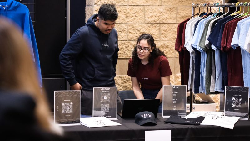 A man and woman working a merchandise table work together on a laptop