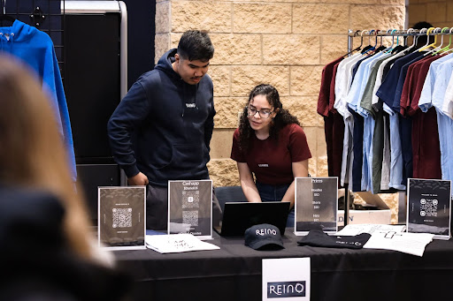 A man and woman working a merchandise table work together on a laptop