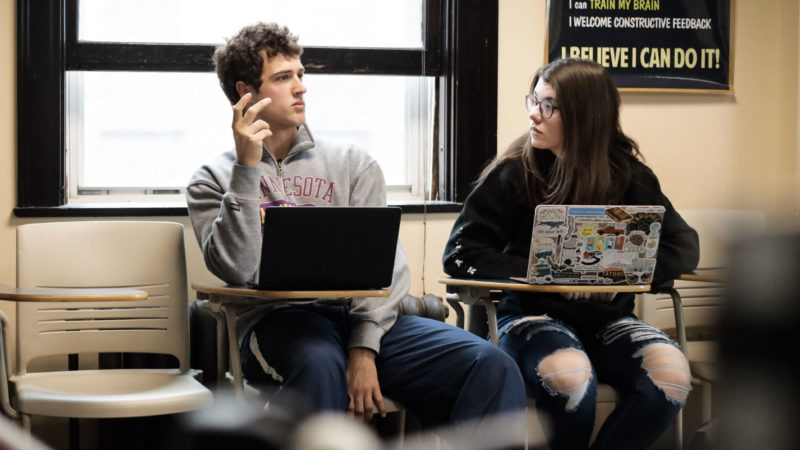 Two students sit next to each other, focused on the classroom conversation