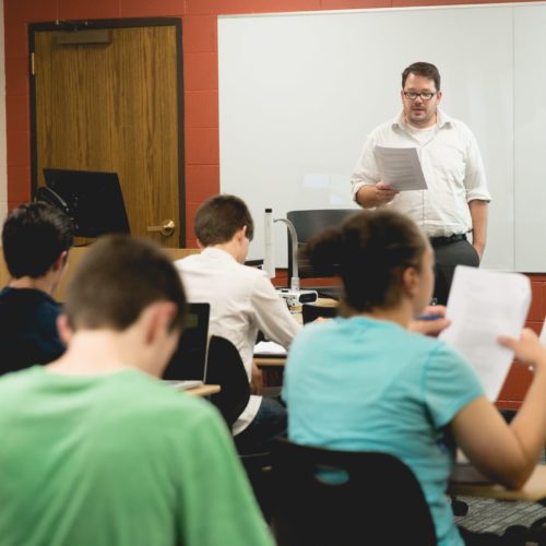 A teacher instructs his class while the studens at their desks follow along