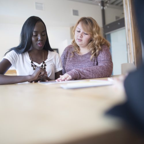 Two women sit at a table reading over music