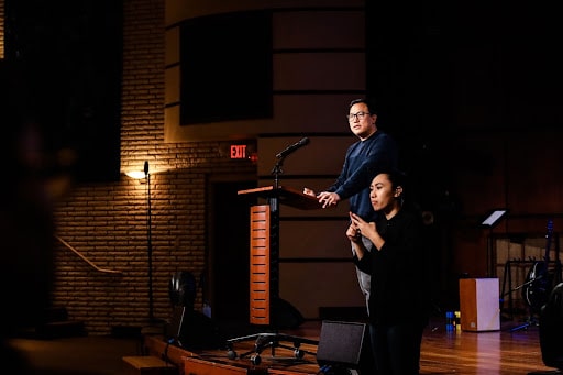 A man speaks on stage with a sign language interpeter translating him for the hearing disadvantaged