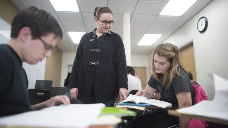 A teacher checks on students are who are studying at their desks in a classroom