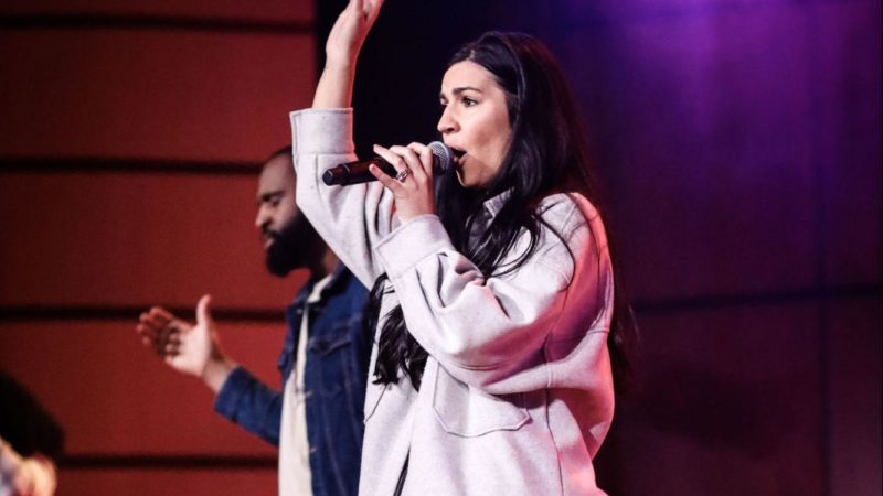 A woman sings on stage leading a group worship