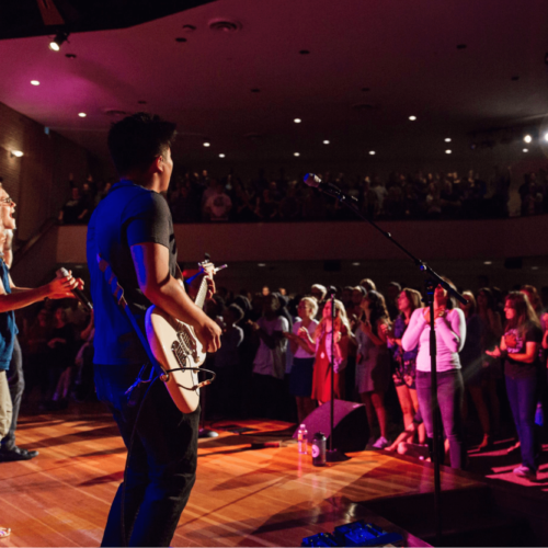 A band performs on stage for a crowded floor and balcony