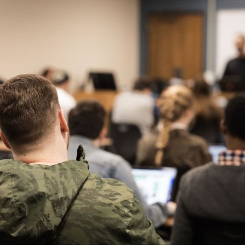 A man watches his teacher in a classroom of attentive students