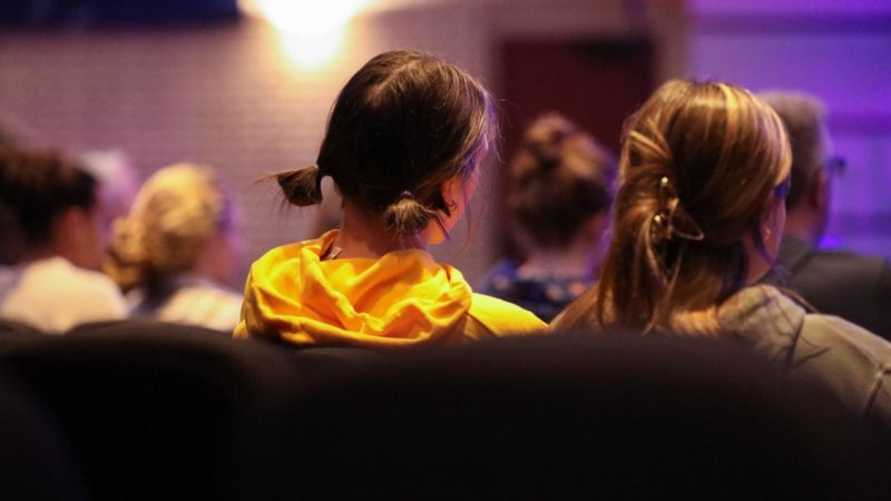 Two women attending theological studies sit next to each other, with other students in the background