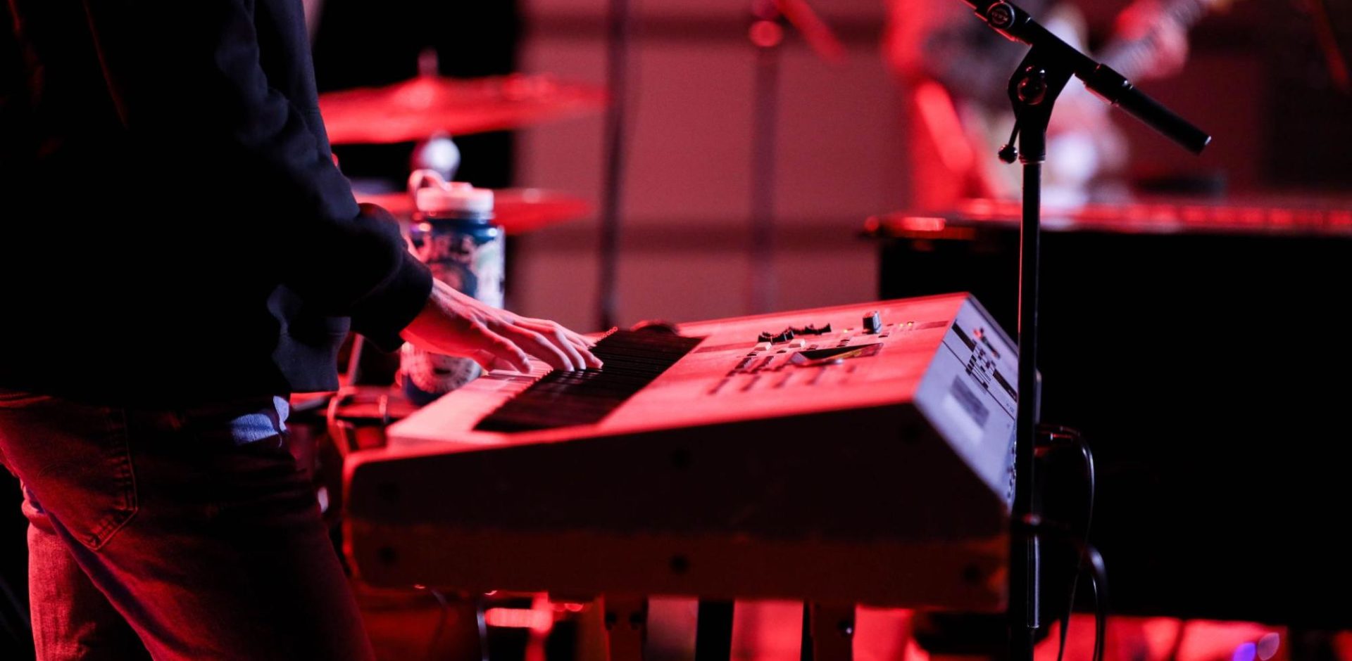 A man plays a keyboard during a live performance with his band in the background