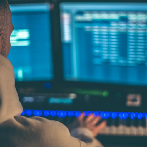 A man plays a MIDI keyboard while producing music on a computer