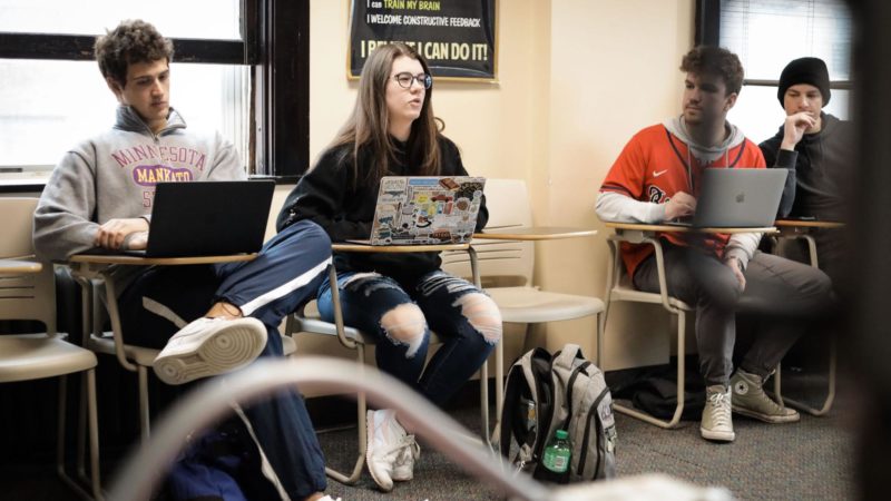 A student sitting up from her laptop speaks to the rest of the class