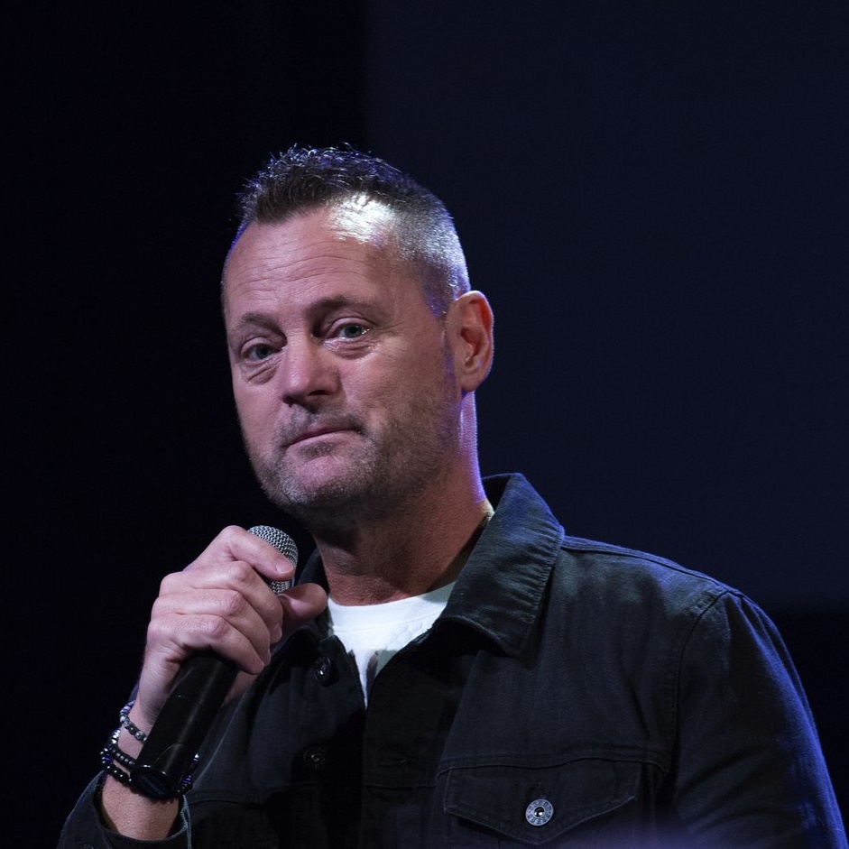 Jeff Grenell holds a microphone and looks into the camera during a pause