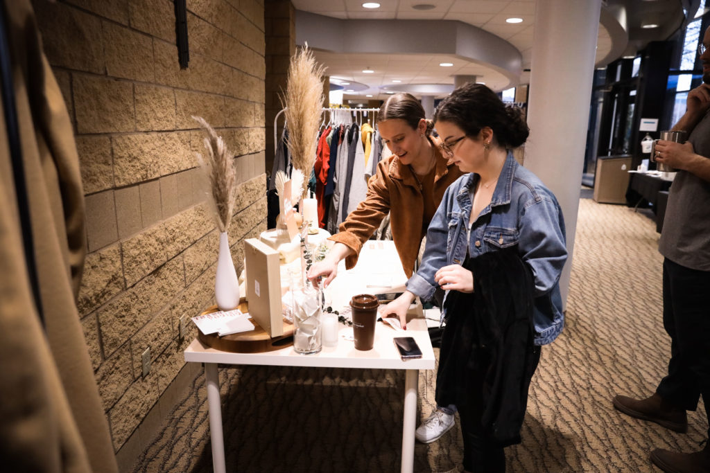 Two women eagerly peruse the items available on a table at a pop-up shop