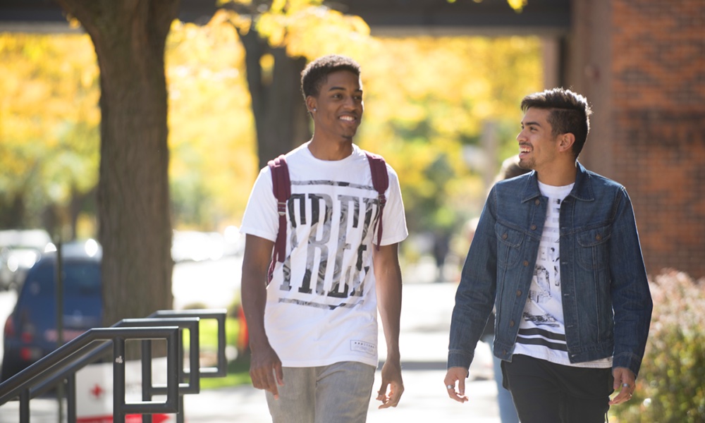 Two students walk down the campus sidewalk, talking and smiling