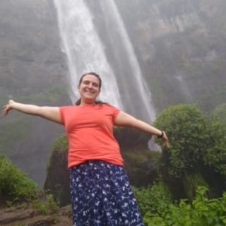 Tirzah smiles and stands with her arms out in front of a waterfall