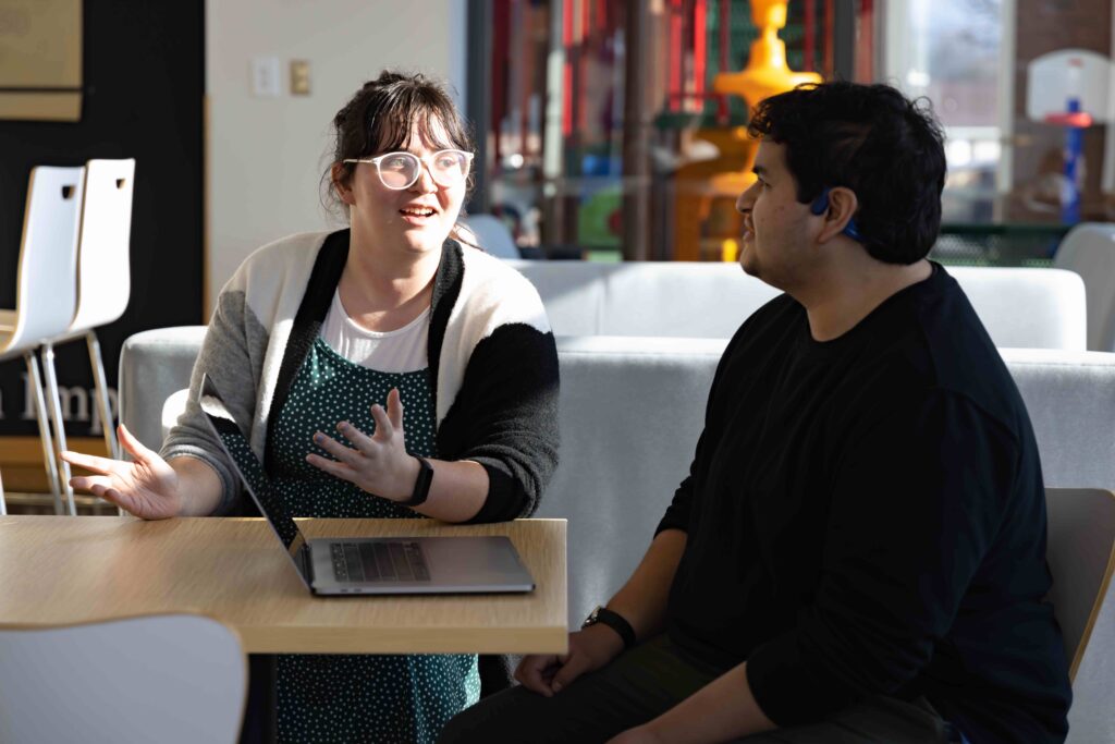 A man and a woman sat at a table speak with each other