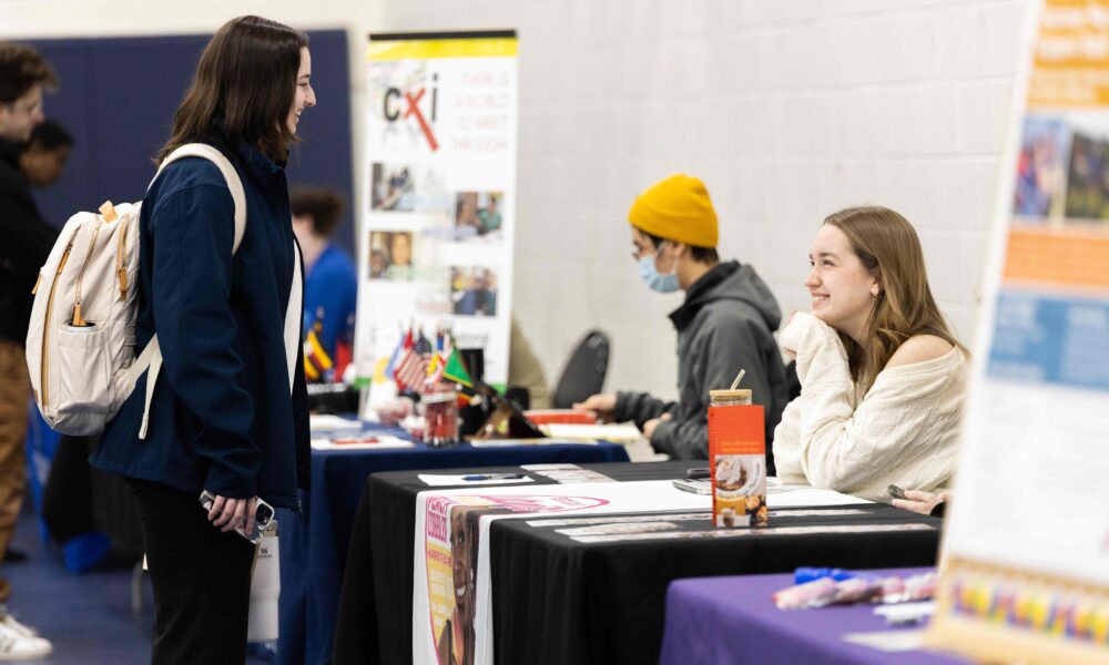 A student seeking information speaks to a vendor at a table