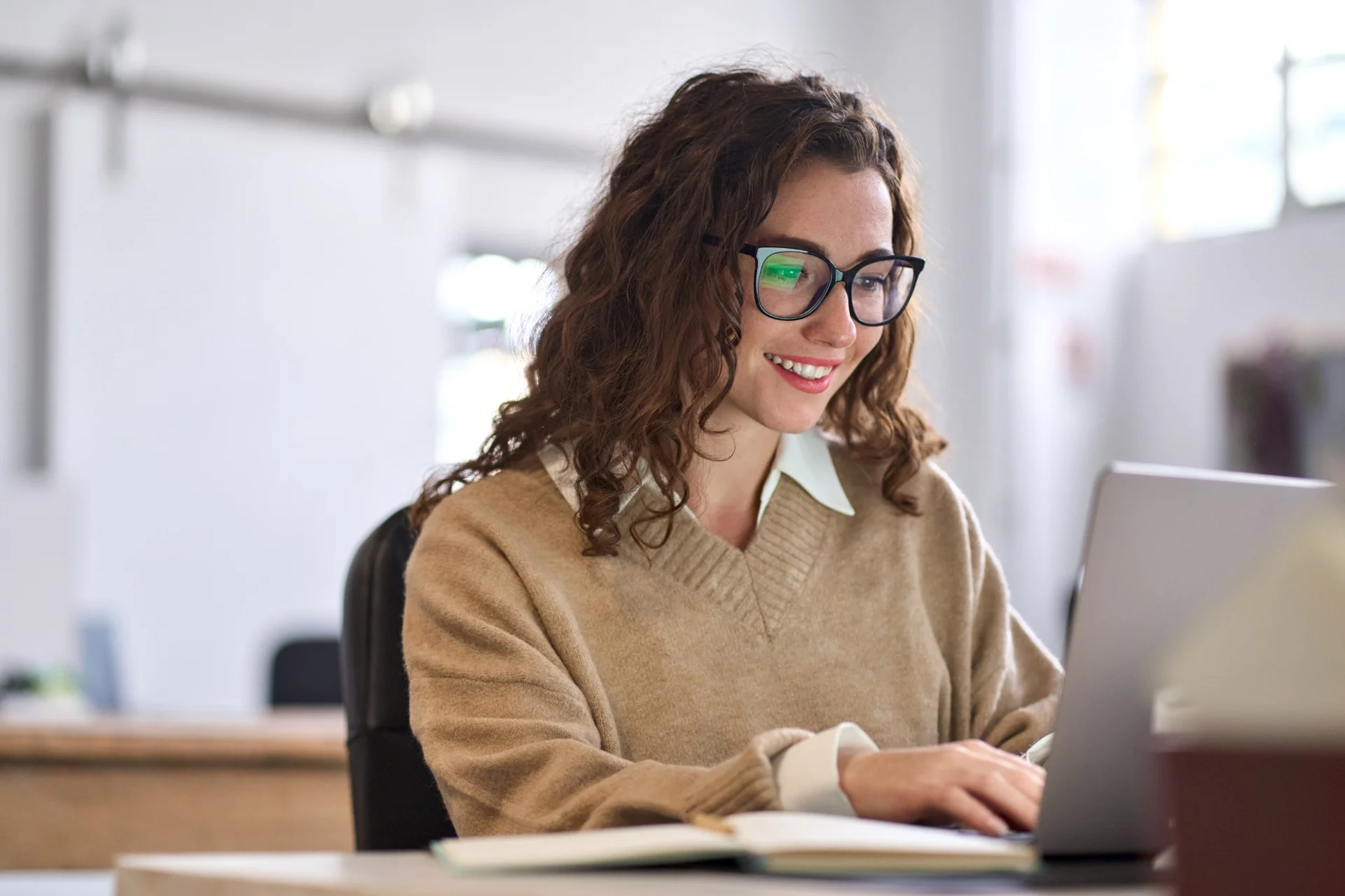Student smiling while working on a laptop in a bright modern office environment